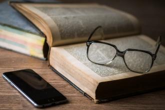 Reading glasses on top of an old book, and a smart phone